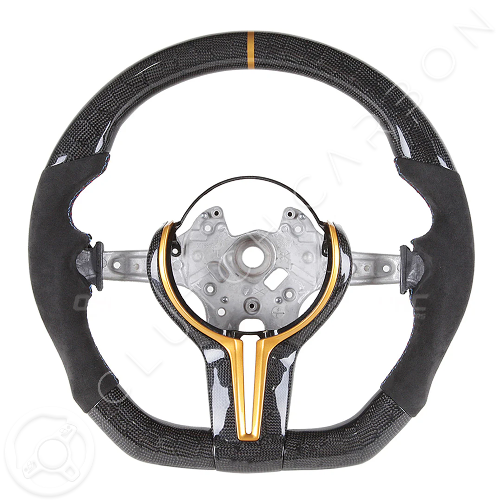 The BMW F-Series Custom Carbon Fiber Steering Wheel is styled with a suede finish, metallic gold center accent, central mounting plate, and an orange stripe atop a white background.