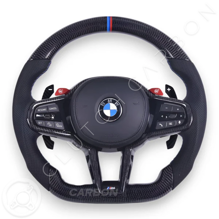 The BMW G-Series LCI Custom Carbon Fiber Steering Wheel boasts a sleek finish, with a center BMW logo, side control buttons, and a distinctive red and blue stripe on top.